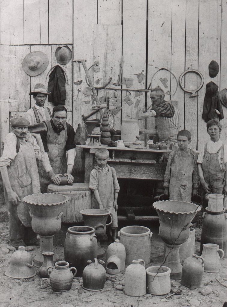 The now famous 1904 Decker Pottery photograph staged outside the pottery showing tools on the wall and finished pieces of pottery. Left to right: William Decker (Uncle Billy), William Duncan, Charles Decker, Jr., a grandson, Charles Sr. at the wheel and two more grandsons. The grandsons, sometimes referred to as apprentices, worked at carrying the pieces to drying racks and other chores. Seen in the Tennessee Conservationist and elsewhere. Burbage2.